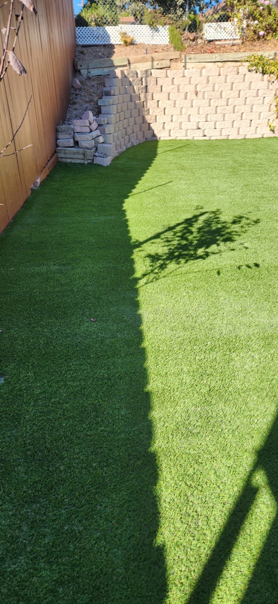 Backyard with new artificial turf and a tan block retaining wall corner